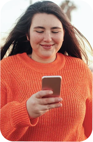 A woman in an orange jumper smiling at her phone