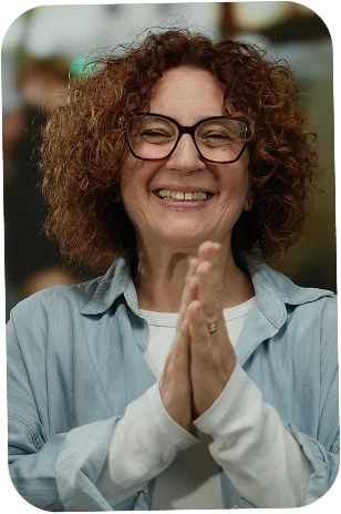 A lady with glasses with her hands clapping together smiling