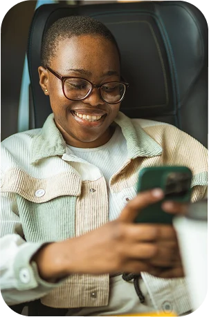 A person with glasses sitting in a black leather chair smiling at their phone