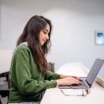 A woman in a green jumper sitting at a table with a laptop