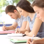 Three people sitting in a row writing in notebooks