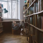 A lady sitting in an armchair reading in a library