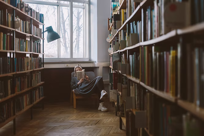A lady sitting in an armchair reading in a library