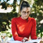 A woman in a red shirt and glasses studying outside