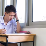 A young man sitting at a small wooden desk studying
