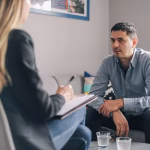 A man sitting across from a female therapists on a grey lounge
