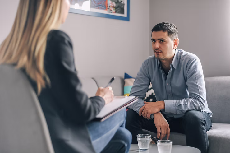 A man sitting across from a female therapists on a grey lounge
