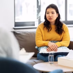 A woman in a yellow top sitting on a lounge at a therapy session