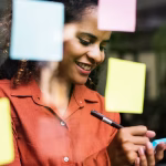 A woman standing at a window writing on a sticky note