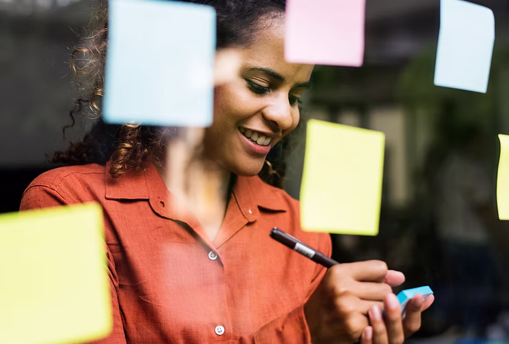 A woman standing at a window writing on a sticky note