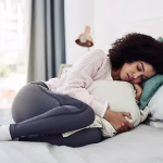 A woman curled up in bed cuddling a pillow appearing upset