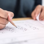A hand filling out an exam paper with a lead pencil