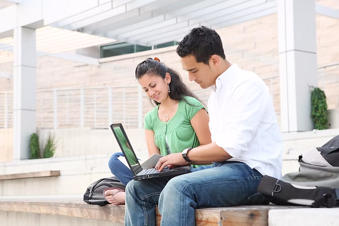 Two people sitting outside studying on a laptop