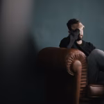 A man sitting on a leather lounge with his head in his hands
