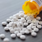A bottle of small pills that has spilt across a table