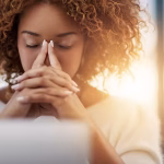 A woman sitting in front of a laptop with her head resting in her hands